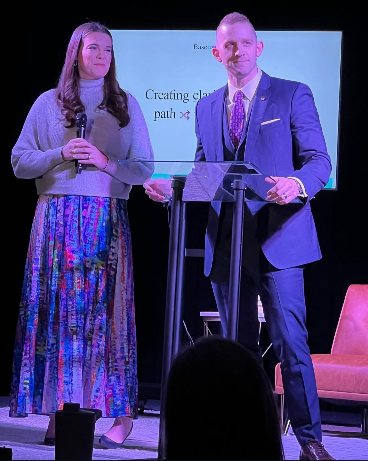Zac and Jill Newell co-presenting on stage at a glass podium